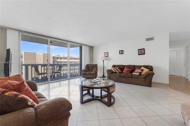 living area with light tile patterned floors, baseboards, visible vents, a wall of windows, and a textured ceiling