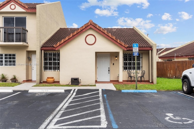 view of front of property featuring uncovered parking, a tiled roof, fence, and stucco siding