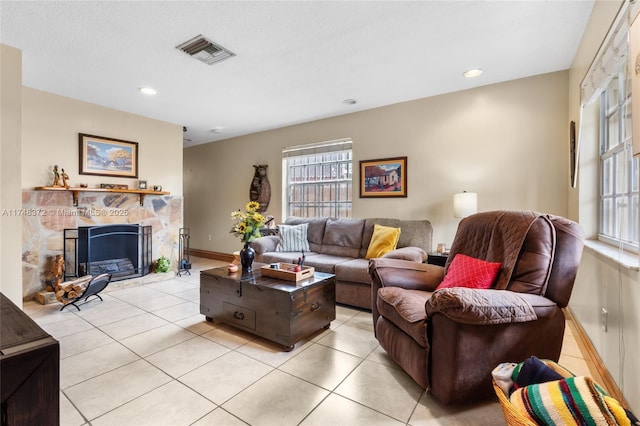 living area with light tile patterned floors, a stone fireplace, visible vents, and baseboards