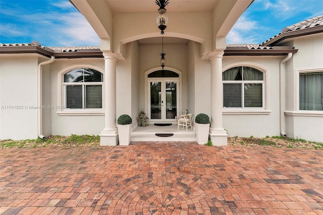 property entrance with a tiled roof, french doors, and stucco siding