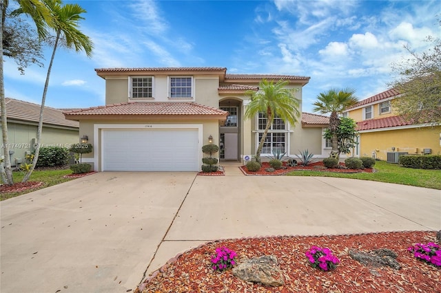 mediterranean / spanish-style home with concrete driveway, a tile roof, an attached garage, central AC, and stucco siding