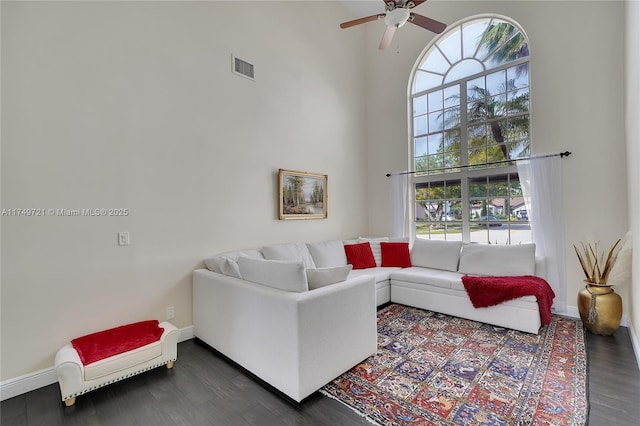 living room featuring dark wood-style floors, baseboards, visible vents, and a high ceiling