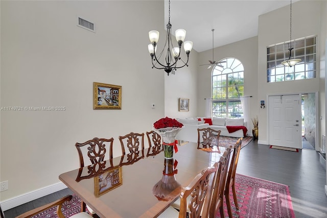 dining space with dark wood-style flooring, visible vents, a towering ceiling, an inviting chandelier, and baseboards