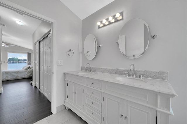 ensuite bathroom featuring lofted ceiling, a water view, a sink, and double vanity