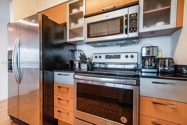 kitchen with light wood-type flooring, appliances with stainless steel finishes, dark countertops, and glass insert cabinets