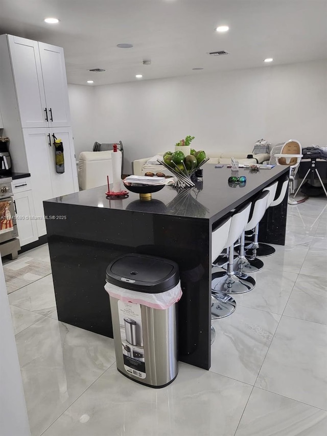 kitchen featuring a breakfast bar area, visible vents, white cabinetry, a center island, and dark countertops