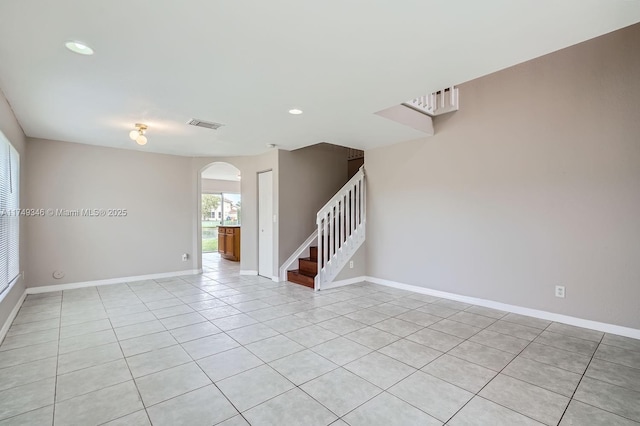 empty room featuring arched walkways, light tile patterned floors, visible vents, baseboards, and stairs