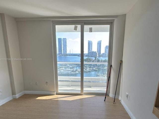 spare room featuring a water view, light wood-type flooring, baseboards, and a city view