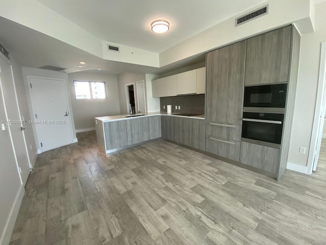 kitchen with black microwave, wall oven, a peninsula, visible vents, and light countertops