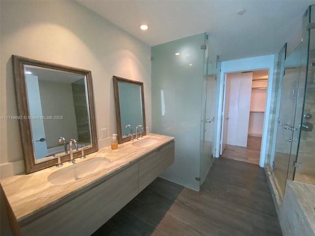 full bathroom featuring a walk in closet, double vanity, a sink, and wood finished floors