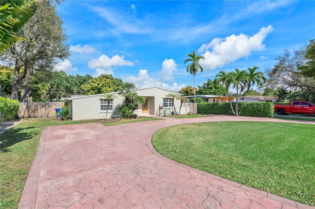 single story home featuring decorative driveway, fence, a front lawn, and stucco siding