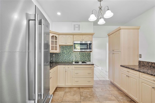 kitchen featuring stainless steel appliances, backsplash, dark stone counters, glass insert cabinets, and pendant lighting