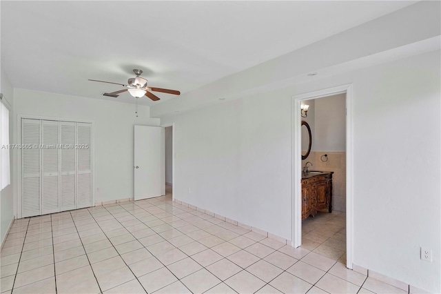 unfurnished bedroom with a closet, light tile patterned flooring, a sink, and a ceiling fan