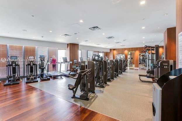 exercise room with recessed lighting, visible vents, wooden walls, and light wood finished floors