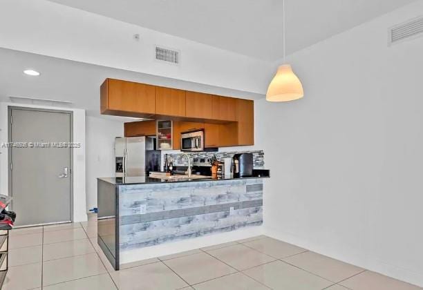 kitchen featuring dark countertops, brown cabinets, hanging light fixtures, stainless steel appliances, and light tile patterned flooring