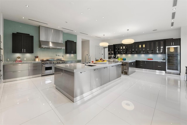 kitchen featuring wall chimney range hood, glass insert cabinets, a large island with sink, and double oven range