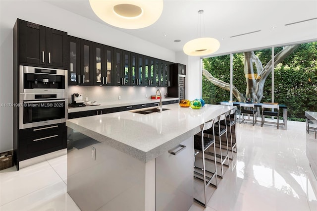 kitchen featuring hanging light fixtures, an island with sink, a sink, and glass insert cabinets