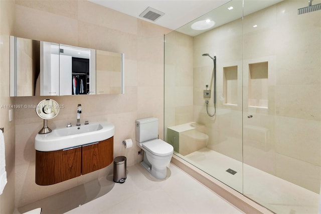 full bath featuring a walk in shower, visible vents, vanity, tile walls, and a spacious closet