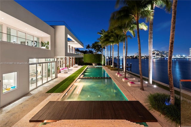 pool at night featuring a pool with connected hot tub and a water view