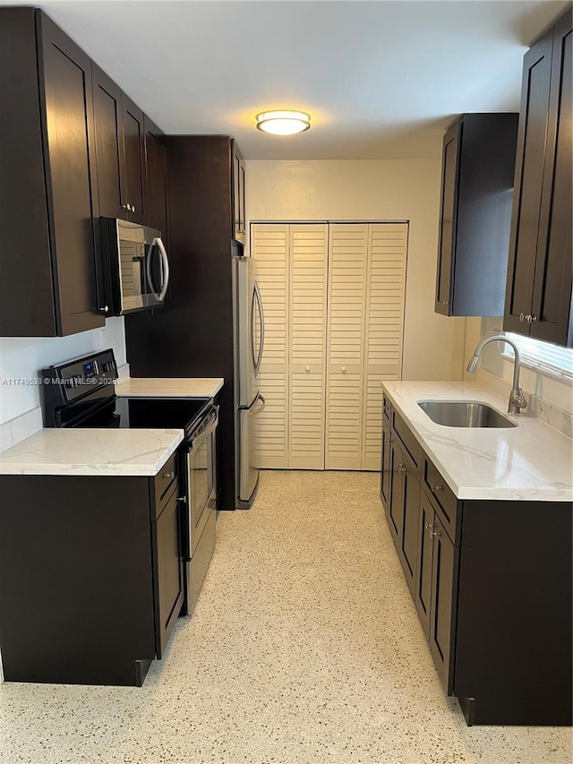 kitchen featuring appliances with stainless steel finishes, a sink, light stone counters, and dark brown cabinets