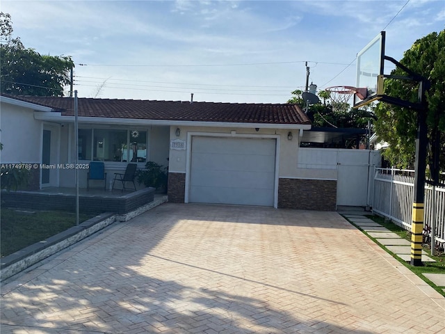 ranch-style home with a garage, a tiled roof, fence, decorative driveway, and stucco siding