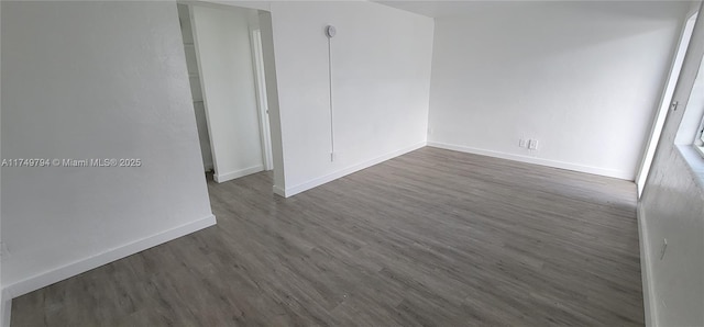 empty room featuring baseboards and dark wood-type flooring