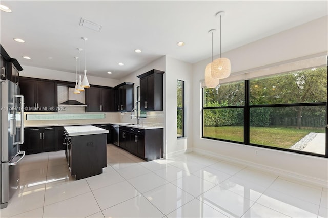 kitchen featuring a center island, light countertops, hanging light fixtures, a sink, and wall chimney range hood