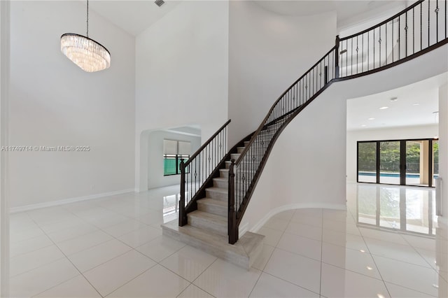 staircase with tile patterned flooring, baseboards, a high ceiling, and an inviting chandelier