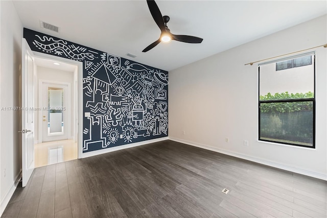 empty room with an accent wall, dark wood-style flooring, visible vents, and baseboards