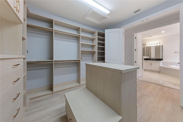 walk in closet with attic access, visible vents, a sink, and light wood-style flooring