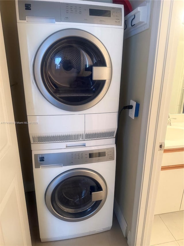 clothes washing area with light tile patterned floors, laundry area, a sink, and stacked washer and clothes dryer