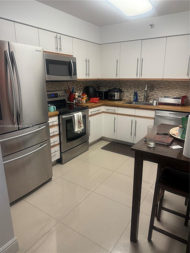 kitchen with light tile patterned floors, a sink, white cabinets, appliances with stainless steel finishes, and tasteful backsplash