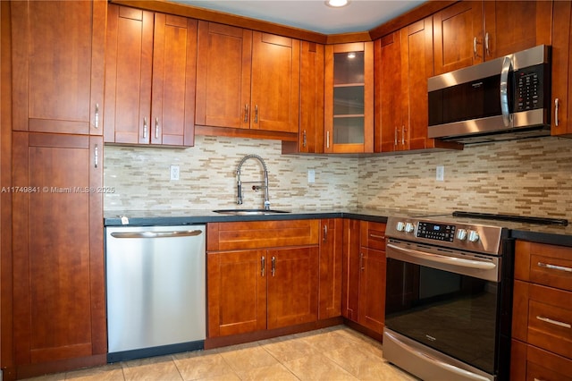 kitchen with decorative backsplash, dark countertops, glass insert cabinets, appliances with stainless steel finishes, and a sink