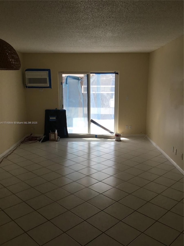 spare room featuring a textured ceiling, a wall mounted AC, tile patterned flooring, and baseboards