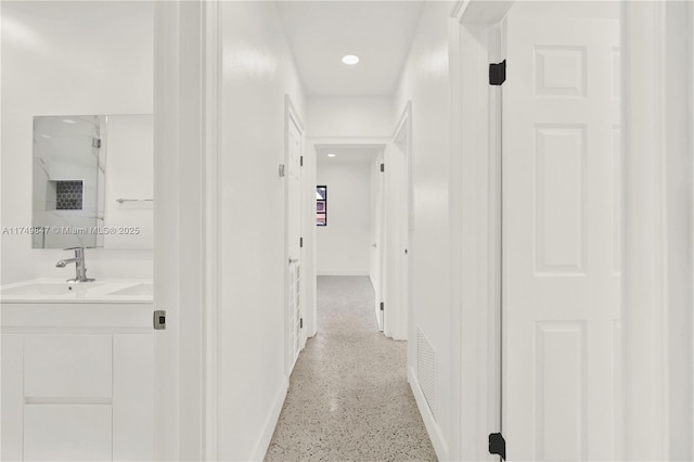 hallway featuring recessed lighting, light speckled floor, baseboards, and a sink