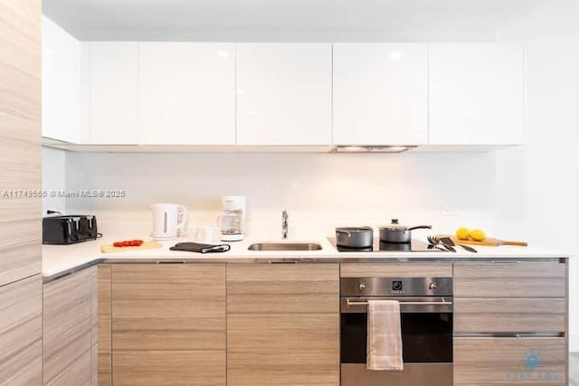 kitchen featuring modern cabinets, white cabinets, a sink, and oven