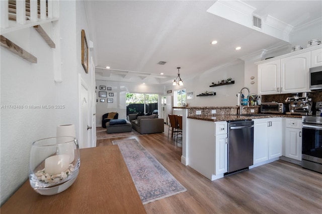 kitchen featuring a peninsula, white cabinetry, appliances with stainless steel finishes, light wood finished floors, and dark stone countertops