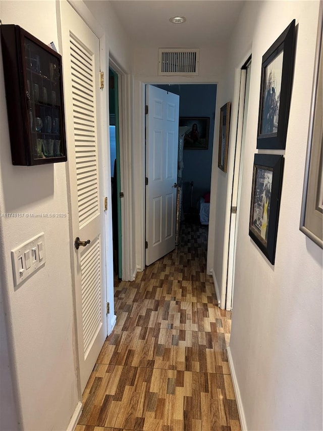 hallway featuring dark wood-type flooring, visible vents, and baseboards