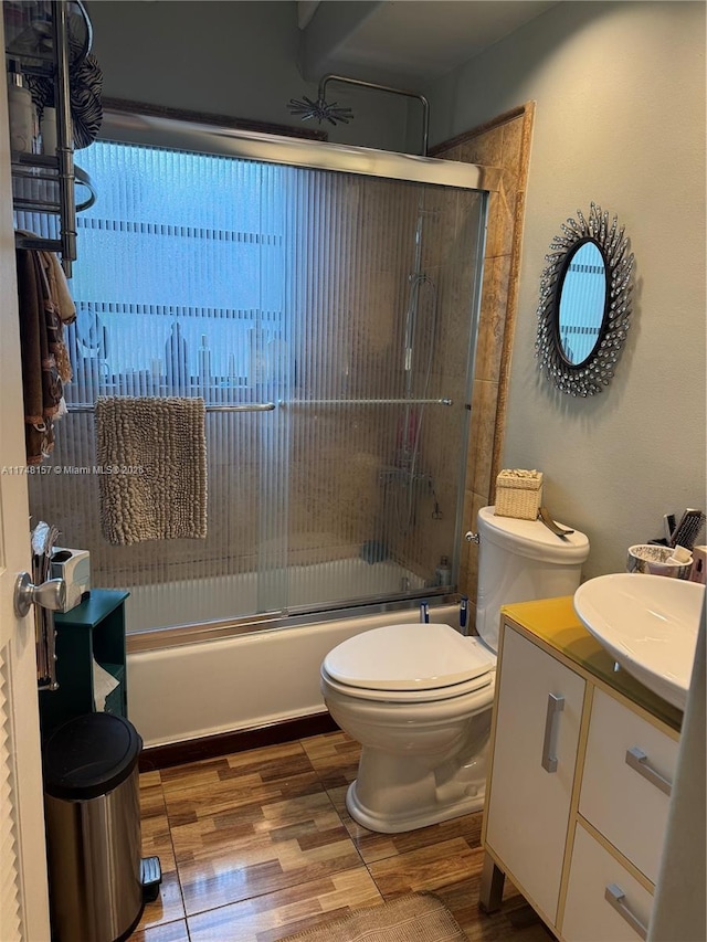 bathroom featuring wood finished floors, vanity, toilet, and bath / shower combo with glass door