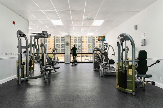 gym with a paneled ceiling, baseboards, and a wall of windows
