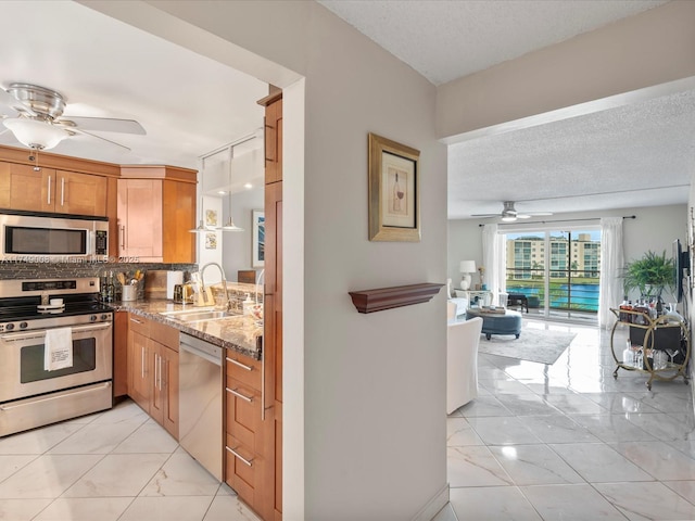 kitchen featuring a textured ceiling, stainless steel appliances, a sink, backsplash, and brown cabinets