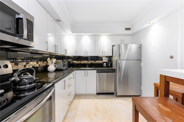 kitchen with white cabinetry, stainless steel appliances, dark stone countertops, and ornamental molding