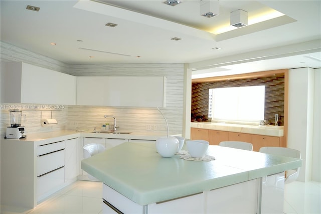 kitchen with a center island, light tile patterned floors, decorative backsplash, white cabinetry, and a sink