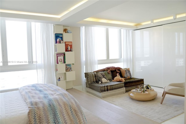 bedroom featuring light wood finished floors, multiple windows, a tray ceiling, and a closet