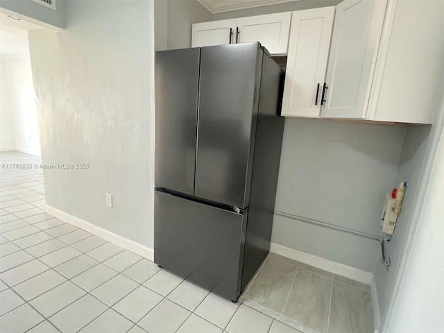 kitchen featuring light tile patterned floors, baseboards, freestanding refrigerator, and white cabinetry