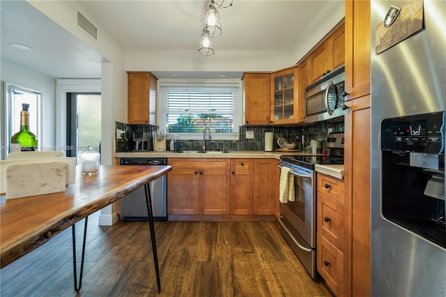 kitchen featuring tasteful backsplash, visible vents, appliances with stainless steel finishes, brown cabinetry, and a sink