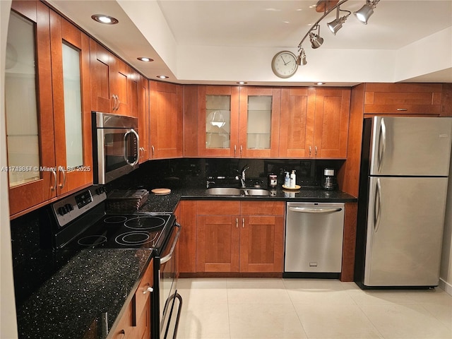 kitchen with tasteful backsplash, dark stone counters, glass insert cabinets, stainless steel appliances, and a sink