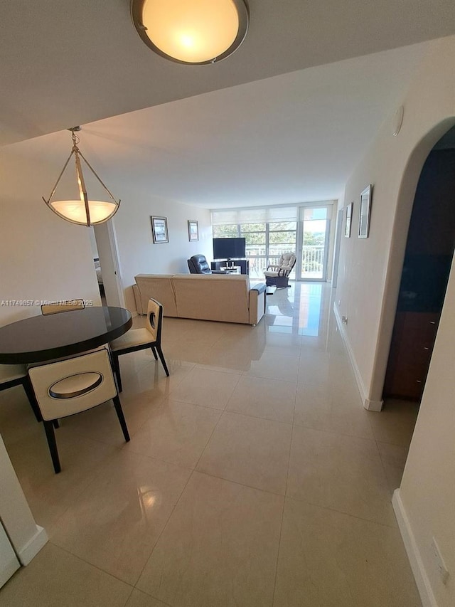 hallway featuring arched walkways, baseboards, and light tile patterned floors