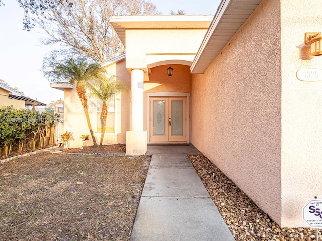 view of exterior entry with stucco siding, fence, and french doors