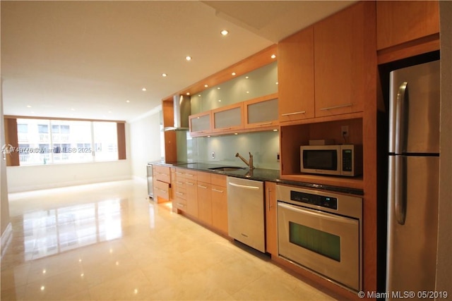 kitchen featuring glass insert cabinets, stainless steel appliances, wall chimney range hood, a sink, and recessed lighting